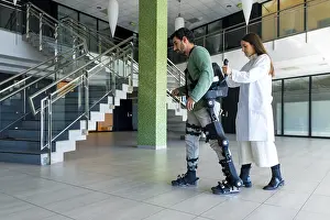 Mechanical Exoskeleton Prints: Mechanical exoskeleton, female doctor physiotherapist walking with disabled person helped by robotic skeleton