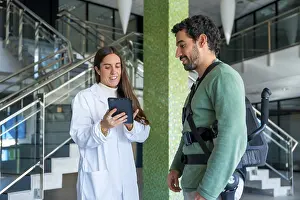 Robotic Skeleton Assistance Prints: Mechanical exoskeleton, female physiotherapist doctor talking with tablet with disabled person with robotic skeleton