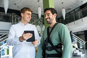 Physiotherapy Equipment Prints: Mechanical exoskeleton, physiotherapist looking at consultation with tablet with disabled person with robotic skeleton