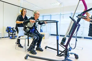 Physiotherapy Equipment Prints: Mechanical exoskeleton. Female physiotherapy medical assistant lifting disabled person with robotic skeleton