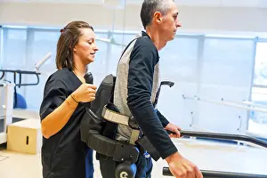 Physical Disability Support Prints: Mechanical exoskeleton. Female physiotherapy medical assistant helping disabled person with robotic skeleton to walk