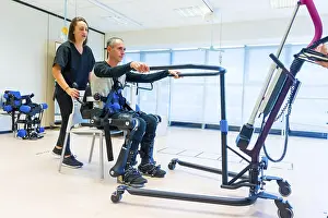 Exoskeleton Technology Prints: Mechanical exoskeleton. Female physiotherapy doctor assistant lifting disabled person with robotic skeleton to get up