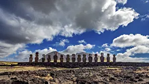 Dramatic Clouds Prints: Moai statues stand under a sky with dramatic clouds on a rocky surface