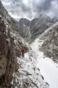 Mountaineer on a rope-secured path in a steep rocky mountain landscape with fresh snow in summer