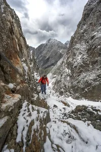 Mountaineer on a rope-secured path in a steep rocky mountain landscape with fresh snow in summer