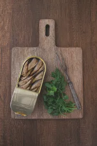 Prints of An open can of sprats, appetizer, on a wooden cutting board, with a fork and herbs, top view Pilchard Prints: An Open Can of Sprats Print, Top View