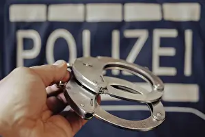 Crime Scene Prints: A pair of handcuffs is held by one hand