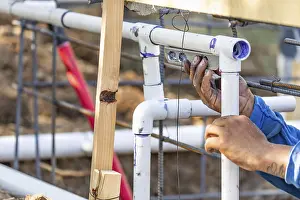 Construction Site Work Prints: Plumber using level while installing PVC pipe at construction site
