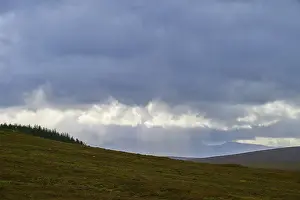 Nature Photography UK Prints: Rays of light break through the clouds above a hill with trees