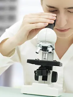 Female Scientist Prints: Scientist looking through a microscope