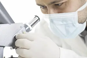 Man In Protective Suit Prints: Scientist watches through a microscope