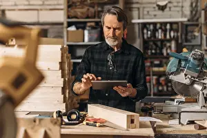 Male Craftsman Prints: Senior carpenter using a digital tablet in his workshop