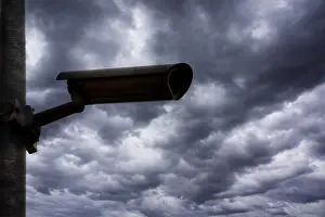Cloudy Sky Photography Prints: Silhouette of a surveillance camera against a dramatic