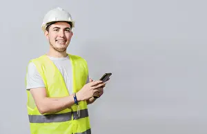 Young Engineer Prints: Smiling engineer using cell phone looking at camera