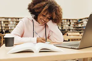 Education And Learning Concept Prints: Smiling student writing in library