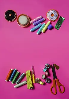 Text Free Space For Copy Prints: Several spools with cotton threads placed with scissors and set of needles on pink surface