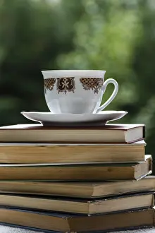 Deserted Garden Table Prints: Stack of books on table in garden with a tea cup on top