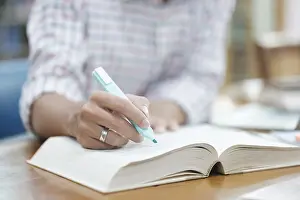 Laptop Computer Use Prints: A student writes notes in a notebook while studying in a library