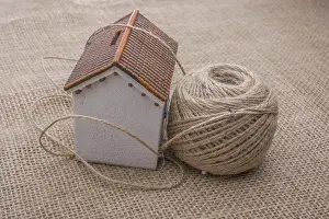 Brown Background Prints: Thread wrapped around a model house on a brown background