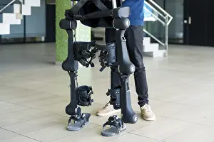 Exoskeleton Technology Prints: Unrecognizable computer engineer in mechanical exoskeleton looking at the robot with a tablet
