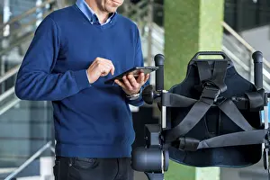 Exoskeleton Technology Prints: Unrecognizable computer engineer in mechanical exoskeleton looking at the robot with a tablet