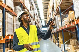 Distribution Warehouse Prints: Side view of an african worker scanning package with bar code reader in a distribution warehouse