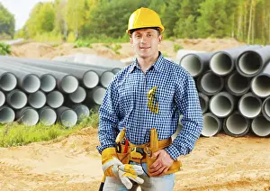 Young Adult Man Prints: Worker near stack of big pipes