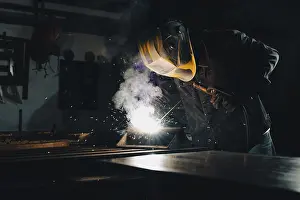 Workplace Safety Equipment Prints: Worker welding an iron plate on the workbench in the workshop