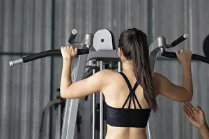 Female Athlete Performance Prints: A young woman performs pull-ups with the help of her trainer